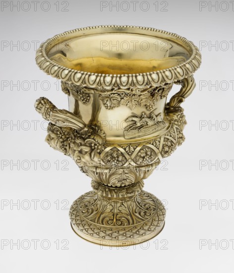 Wine cooler by Boulton & Plate Co. Birmingham; goldsmith and plater firm; fl. 1768–1834. Classicist, Georgian style, 1826/1827. Silver vessel, height 30 cm, width 27 cm, depth 24.5 cm, weight 3725 g. Decor: vine ornament, acanthus leaves, cymatium, decorative strip of vines under the upper edge, stylized kimation on the rim; body on a circular foot decorated with a half-cylinder of laurel and acanthus leaves overlapping a short stem; lower body enclosed with large acanthus leaves, upper body decorated with vines in a diagonal rhombic braid. Plaque with horse racers on the front; a plaque with a secondary inscription in Cyrillic script attached to the back original inscription, probably referring to a prize in horse races, has been erased. Massive handles mounted in satyr masks; satyr heads; jockey on horse, horse racing iconography; corporate mottoes and maker's mark., A large ornate metal vessel with a polished golden surface featuring an open rounded rim with a beaded and scalloped e...
