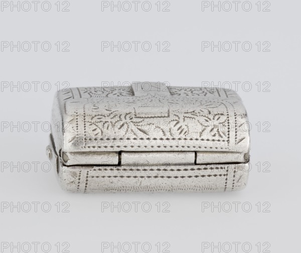 Fragrance container vinaigrette in the form of a bag with an envelope closure and a protruding tongue, decorated on the front with dot-engraved flowers and leaves. Hinged lid opens to an interior openwork insert decorated with plant scrolls. Scraps; engraved; bag shape; toilet accessory. Maker: Thomas Shaw fl. 1822–ca. 1840; 1782–1845. Date: 1834/1835. Materials: goldsmith work. Dimensions: height 2.1 cm, width 1.5 cm, depth 1 cm, weight 10 g. Place: Birmingham, England, Great Britain., A small rectangular metal box with a hinged lid, shown from the front on a plain light gray background. The box has an embossed decorative pattern of floral and geometric motifs across its surfaces, with dotted border lines and textured engraving. The metal appears silver in color with areas of subtle dark tarnish and wear that accentuate the etched details. The hinge is visible along the front edge and the lid has a slightly raised central tab. The overall shape is compact with rounded corners and a sm...