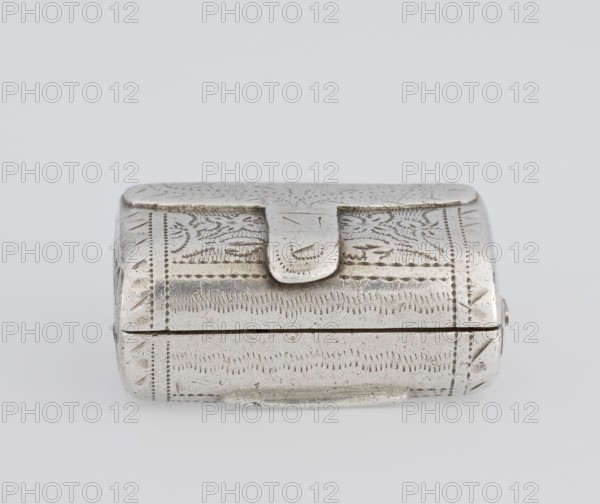 Fragrance container vinaigrette in the form of a bag with an envelope closure and a protruding tongue; front decorated with dot-engraved flowers and leaves. Hinged lid opening to an inner openwork insert decorated with plant scrolls. Scraped/purchase, Maker: Thomas Shaw fl. 1822–ca. 1840; assc. dates 1782–1845. Dated 1834/1835. Material: goldsmith work. Function: toilet accessory. Place: Birmingham, England, Great Britain. Dimensions: height 2.1 cm, width 1.5 cm, depth 1 cm; weight 10 g., A small rectangular metal box with rounded edges and a hinged lid sits on a pale background; the box has an overall silver-gray color with areas of darker tarnish and fine surface scratches, and its exterior is decorated with engraved linear and dot patterns creating banded motifs and subtle leaflike shapes. The lid features a short tab that overlaps the front edge and shows similar engraved marks and wear. The sides and front display repeating incised strokes and dotted borders, and the bottom edge s...