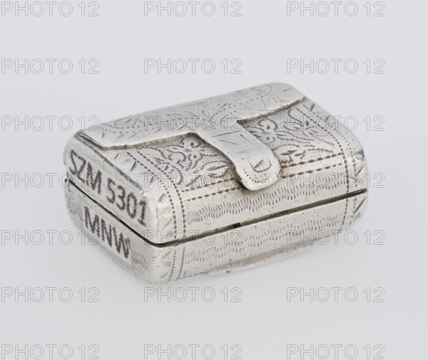Fragrance container vinaigrette, maker: Thomas Shaw fl. 1822–ca.1840; 1782–1845, scrap - purchase, purchase provenance. Vinaigrette in the form of a bag with an envelope closure and a protruding tongue; front decorated with dot-engraved flowers and leaves. Opening box with hinged lid; interior openwork insert decorated with plant scrolls. Date: 1834/1835. Materials/technique: engraved metal goldsmith. Function: toilet accessory. Place: Birmingham, England, Great Britain. Dimensions: height 2.1 cm, width 1.5 cm, depth 1 cm; weight 10 g., A small rectangular metal box with rounded corners sits on a pale background, showing an embossed decorative pattern across its top and sides and a raised tab-like clasp on the lid; the surface appears worn with slight scratches and darker tarnished areas, and the visible colors are silver and grey.