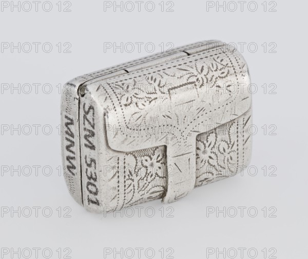 Fragrance container vinaigrette, 1834/1835. Silver vinaigrette in the form of a bag with an envelope closure and a protruding tongue, decorated on the front with dot-engraved flowers and leaves. Hinged lid opens to reveal an openwork insert decorated with plant scrolls. Engraved, bag shape; toilet accessory. Maker: Thomas Shaw fl. 1822–ca. 1840; 1782–1845. Birmingham, England. Height 2.1 cm; width 1.5 cm; depth 1 cm; weight 10 g., A small rectangular metal box with rounded edges sits against a light gray background; the box is silver in color with visible areas of darker tarnish and fine scratches, and its surface is covered in engraved floral and dotted decorative patterns. There is a hinged lid with a protruding clasp on the front, and the engraved motifs include leaf-like shapes and small curved details. The metal shows a mix of bright silver and duller gray tones, with some areas appearing slightly darker where the engraving and wear are deepest.
