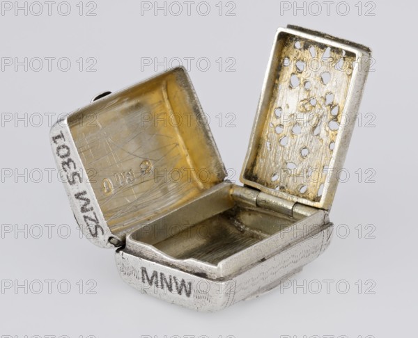 Fragrance container vinaigrette, maker: Thomas Shaw fl. 1822–ca. 1840; 1782–1845, goldsmith. Scrap - purchase; provenance: purchase. Vinaigrette in the form of a bag with an envelope closure and protruding tongue, front decorated with dot-engraved flowers and leaves. Hinged lid opens to an interior openwork insert decorated with plant scrolls. 1834/1835. England, Birmingham, Great Britain. Toilet accessory. Materials/technique: engraving, openwork. Dimensions: height 2.1 cm, width 1.5 cm, depth 1 cm; weight 10 g., A small open metal box with a hinged lid shown from an angled top view, revealing an interior with a worn golden surface and a few scratched areas; the exterior is silver-colored with a slightly textured finish and darker tarnished spots; the underside of the lid has a perforated panel with irregular holes and a gold-toned surface around them; the hinge and inner rim show metallic wear with a mix of gold and silver tones; the background is a smooth light gray.