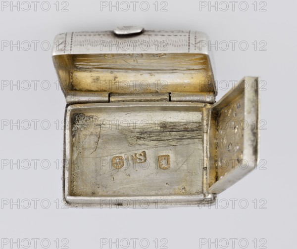 Fragrance container vinaigrette. Maker: Thomas Shaw fl. 1822–ca. 1840; 1782–1845, goldsmith. Scrap - purchase, purchase provenance. Vinaigrette in the form of a bag with an envelope closure and a protruding tongue, decorated on the front with dot-engraved flowers and leaves. Hinged lid opens to reveal an openwork insert decorated with plant scrolls. Materials/technique: engraving, openwork. Date: 1834/1835. Place: Birmingham, England, Great Britain. Function: toilet accessory. Dimensions: height 2.1 cm, width 1.5 cm, depth 1 cm; weight 10 g., A small rectangular metal box with its lid open, showing an inner surface with worn and scratched areas; the interior has a mix of silver and warm gold tones with patches of darker tarnished spots, and the exterior edges appear silver with engraved patterns on the lid. The hinge and inner rim show metallic wear, and the inner side of the lid displays horizontal scratch marks and a golden wash; the right side panel of the box is open and reveals a ...