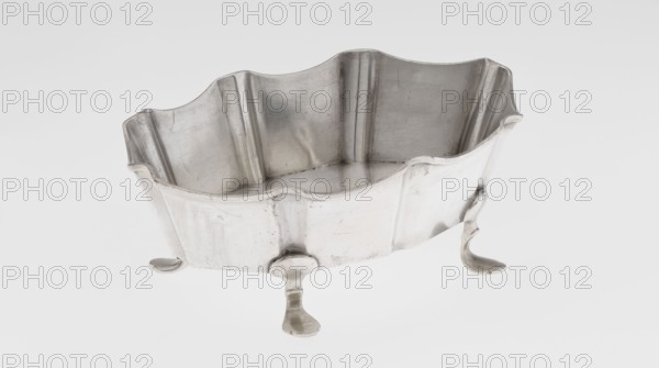 Vase by Mappin & Webb Ltd goldsmith, silversmith, dealer; fl. 1859-. Oblong silver vase, vertically ribbed with a wavy-cut edge, supported by four curved legs. Inscription/marking: Mappin & Webb Ltd maker. Made 1901–1902, London, England. Vessel; height 6 cm, width 15.5 cm, depth 10.5 cm; weight 173 g., A metallic, scalloped-edged container with a wavy rim sits on three curved legs, showing a reflective, slightly scratched silver surface with variations of gray and hints of white highlights; the interior walls display vertical ridges and a smooth base, and the exterior shows subtle dents and worn areas with darker gray shadows around the legs and inner corners.