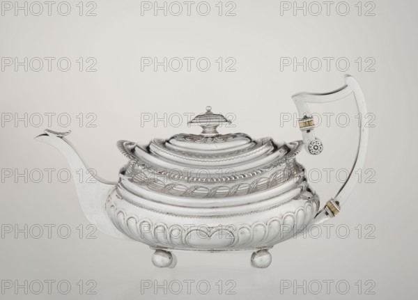 Teapot by George McHattie fl. 1799–ca. 1825, English Regency style, 1819–1820, Edinburgh, Scotland. Rectangular teapot with rounded edges supported by four ball feet; decorated with hoardings ornament at the bottom and two smooth half-cylinders above, with an engraved braid band at the narrowing. Upper edge has a collar decorated with hoardings and flowers. Hinged, rectangular profiled lid edged with tendril; spout-shaped spout set high on the axis. Broken ear with bone insulators. Materials: silver vessel. Dimensions: height 16 cm, width 28.5 cm, depth 13.5 cm; weight 735 g., A polished silver teapot sits against a pale neutral background, showing a rounded body with ornate raised patterns and scalloped edging, a domed lid with a small finial on top, a long curved spout on one side and a tall angular handle on the other with small decorative bands, and the teapot rests on a few spherical feet; visible colors include silver tones, touches of gold on the handle bands, and the soft beige...