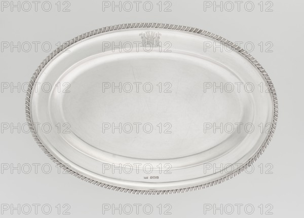 Oval platter by Mappin & Webb Ltd goldsmith, silversmith, dealer; fl. 1859–, oval platter with smooth mirror and slightly raised collar surrounded by a godron half-cylinder; on the collar a four-field coat of arms under an earl's coronet; godron ornaments, rank crowns heraldry. Dated 1904–1905. England; Sheffield, Great Britain. Dish. Materials implied: silver/goldsmith work. Height 2 cm; width 33 cm; depth 22.5 cm; weight 625 g., A large oval metal tray with a raised rim and a twisted rope-like decorative edge, shown against a pale gray background; the tray surface is smooth and slightly reflective with visible fine scratches and wear, and the overall colors are silvery gray and light gray.