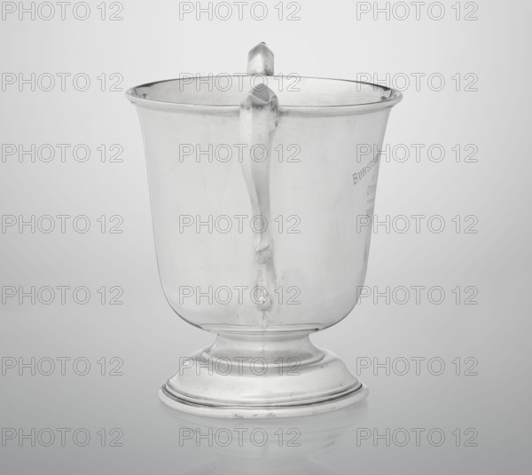 Prize cup by Mappin & Webb Ltd goldsmith, silversmith, dealer; fl. 1859– — cup on a circular, arched, profiled base with a short shaft; semi-ovoid body flattened at the bottom; slightly flared upper edge bordered with a half-cylinder; two volute handles on the sides. Engraved inscription: BURSTON POINT TO POINT MEETING / 22nd APRIL 1911 / OPEN STEEP LECHASE / WON BY / MR H.DETERDING'S / NIGGER, 1910/1911. England, London. Vessel; height 16.5 cm, width 23.5 cm, depth 14.5 cm, weight 500 g., A reflective metallic cup with a smooth curved body sits on a rounded pedestal base; the cup has a single vertical handle attached to its side and a slightly flared rim, and the surface shows faint marks and reflections. The visible colors are silver, gray, and white.
