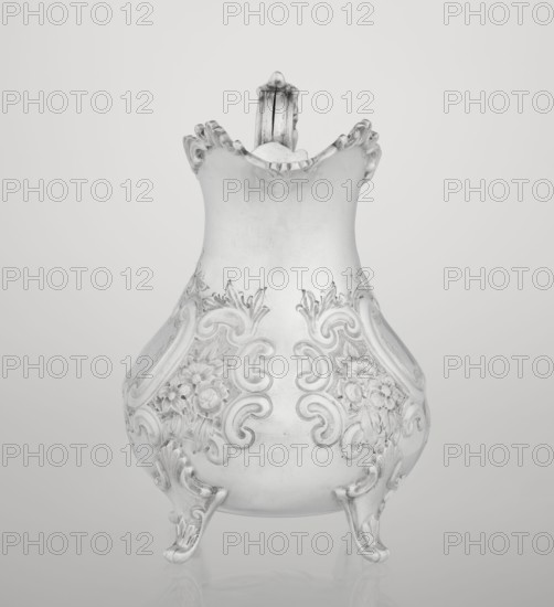 Milk jug, goldsmith/silversmith/dealer Mappin & Webb Ltd fl. 1859– maker, scrap - neo-rococo style, rocaille ornament, flowers, channel-shaped jars ornament, acanthus leaves ornament; pear-shaped milk jug supported on four volute legs, decorated with an acanthus leaf at the base, decorated on the belly with rococo motifs in the form of channel-shaped jars, rocailles and flowers and acanthus leaves; volute handle with acanthus projections and a wide, raised spout with a serrated edge; 1895–1896; Sheffield, England, Great Britain; vessel; height 14.4 cm, width 9.5 cm, depth 8.5 cm, weight 266 g, A decorative pitcher with an ornate, curving silhouette sits against a plain background, displaying a smooth upper body that flares into a scalloped rim and a detailed handle rising from the back; the lower body features embossed floral and scrollwork patterns and rests on three cabriole-style feet with curled toes. The visible colors are shades of gray, silver, white, and off-white.