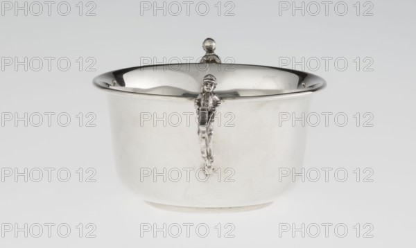 Porridge bowl porringer, goldsmith/silversmith maker, cylindrical bowl with a flat bottom, slightly widening toward the top with a turned-up edge edged by a smooth half-cylinder. Two side handles formed as figurines of boys in jockey outfits riding toy horses on sticks. Inscription/marking by maker. Function: porridge/porringer; subject: jockeys, children's games, toy horses. Date: 1935–1936. Place: Sheffield, England, Great Britain. Dimensions: height 5.6 cm; width 16.3 cm; depth 10.5 cm; weight 125 g., A shiny metal bowl with a rounded rim and a reflective interior sits against a pale gray background, showing a small decorative figure attached to its front that extends downward along the bowl's surface; the bowl and figure display metallic silver and gray tones with subtle darker reflections and highlights, and the overall scene includes white and light gray areas from reflections and the backdrop.