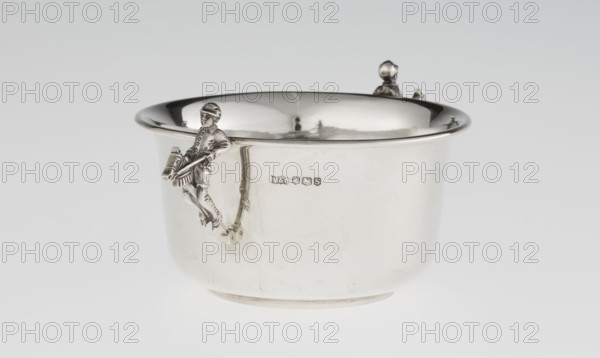 Porridge bowl porringer by Mappin & Webb Ltd goldsmith, silversmith, dealer; fl. 1859–. Cylindrical bowl with a flat bottom, slightly widening toward the top, with a turned-up edge edged by a smooth half-cylinder. Two side handles in the shape of figurines of boys dressed in jockey outfits, riding toy horses on sticks. Associated themes: jockeys, children's games, porridge. Material/function: vessel/porridge dish. Date: 1935–1936. Place: Sheffield, England, Great Britain. Dimensions: height 5.6 cm; width 16.3 cm; depth 10.5 cm; weight 125 g., A shiny silver bowl with a rounded rim and smooth curved sides sits against a light gray background, featuring a small sculpted figure attached to the side holding a drum and drumsticks and another small sculpted head peeking over the rim; the surface reflects highlights and shadows, showing metallic silver and soft gray tones with faint darker reflections.
