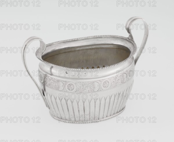Sugar bowl by Hutton & Sons Ltd Sheffield, Birmingham, London; goldsmith and silversmith firm; fl. 1800–1930. Silver sugar bowl, oval with two ribbon handles; clasp vertically in the lower section; decorated above with a band of stylised acanthus twig; upper edge decorated with a godron half-cylinder. Godron ornaments, plant twig motif. Dated 1895/1896, London, England. Vessel; height 11 cm, width 17.3 cm, depth 10.5 cm, weight 231 g., A metal vessel with a reflective silver surface and a shallow oval opening sits against a plain light background; it has a pair of curved handles rising from opposite sides, ornate edging around the rim, decorative embossed banding with floral and circular motifs around the upper body, and vertical fluted panels along the lower body, while the interior shows a slightly darker, warm metallic tone; visible colors include silver, gray, light beige, and subtle warm brown tones.