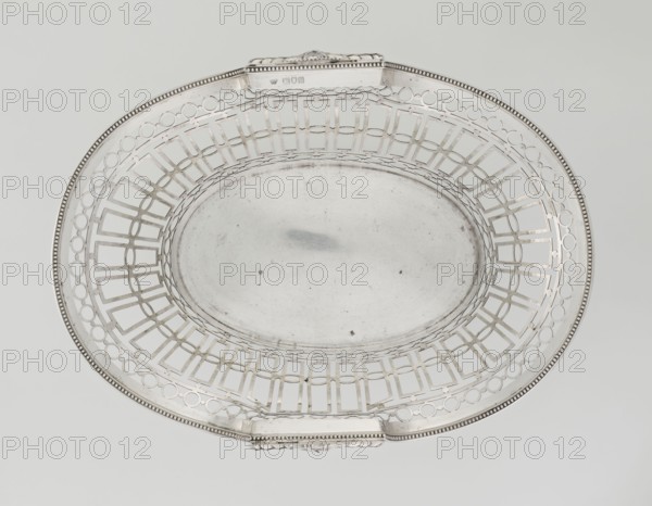 Fruit Basket, Mau, Hainrich fl. early 20th century maker ; Hutton & Sons Ltd Sheffield, Birmingham, London; goldsmith and silversmith firm; fl. 1800-1930 maker. Openwork, neoclassicism; geometric ornaments; garlands; pearling. Neoclassical openwork oval basket supported on four volute legs. Openwork formed by bands of ovals, circles and rectangles; top and bottom edges bordered with pearling. Raised sides topped on the shorter axis by a semi-plastic vase with laurel leaf garlands. Engraved on the bottom with an italic inscription: 6. September / 1893 1918 / von CP Dietz, 1908/1909. England, London. Vessel; height 8.5 cm, width 35.5 cm, depth 25 cm, weight 925 g., A decorative oval metal tray with an open lattice rim and a solid central well, shown from above; the tray has a beaded edge and two small raised rectangular handles on opposite sides, and the surface shows some subtle scratches and spots. The visible colors are silver, gray, and off-white.