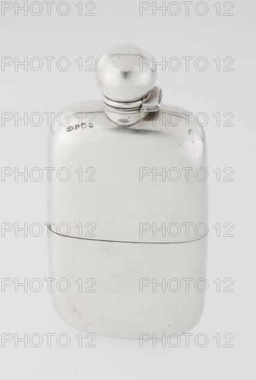 Hip flask by Unite, George & Sons Birmingham; goldsmith's firm; fl. 1825–1928. So-called cuboid hip flask with rounded corners; smooth, slightly curved; spout in the form of a narrow neck with an applied spherical hinged stopper; bottle narrowed in the lower part from the middle; on this part a slide-in container — a cup masking the narrowing is placed; the interior of the cup and the spout are gilded. 1907/1908, England; Birmingham, Great Britain. Materials/function: alcohol vessel/alcohol bottle. Height 15.5 cm, width 7.6 cm, depth 2.7 cm, weight 240 g., A smooth, reflective metal flask with a rounded rectangular body and a spherical screw cap attached by a small hinge, showing a shiny silver surface with subtle scratches and scuff marks, set against a light gray background.