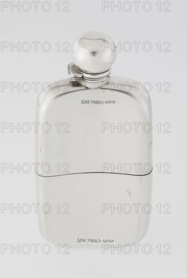 Hip flask, George & Sons Birmingham, goldsmith's firm, fl. 1825–1928. So-called cuboid hip flask with rounded corners; smooth, slightly curved body; spout formed as a narrow neck with an applied spherical hinged stopper; bottle narrowed in the lower part from the middle; on this part a slide-in container — a cup masking the narrowing — is placed. Interior of the cup and the spout are gilded. 1907/1908. England, Birmingham, Great Britain. Vessel. Height 15.5 cm, width 7.6 cm, depth 2.7 cm, weight 240 g. Purchase provenance; scrap - purchase; alcohol vessel; alcohol bottle., A smooth reflective metal flask with a rounded top and a hinged spherical cap sits against a light gray background, showing a polished silver surface with subtle scratches and small scuff marks; the flask appears in two joined sections with a thin darker seam between them, and the visible colors are silver, gray, and hints of darker gray in the reflections.