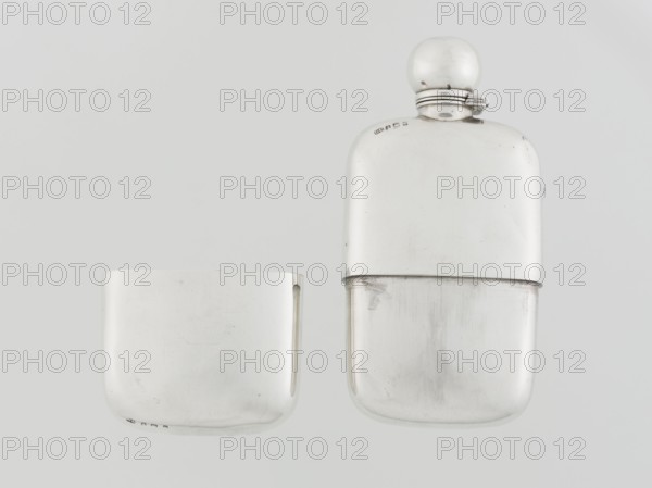 Hip flask, George & Sons Birmingham; goldsmith's firm; fl. 1825–1928. So-called cuboid hip flask with rounded corners; smooth, slightly curved; spout in the form of a narrow neck with an applied spherical hinged stopper; bottle narrowed in the lower part from the middle; on this part a slide-in container — a cup masking the narrowing — is placed; the interior of the cup and the spout are gilded. Alcohol vessel, 1907–1908. England, Birmingham. Height 15.5 cm, width 7.6 cm, depth 2.7 cm; weight 240 g., A photograph of a metallic hip flask and its matching cup, both shown against a pale gray background; the flask has a rounded rectangular shape with a smooth reflective surface and a spherical cap attached by a small hinged collar, and the cup is a shorter rounded rectangle with a similar smooth reflective finish; visible colors are silver, light gray, and subtle darker gray reflections across the surfaces.