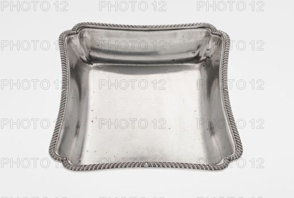 Four-sided platter by Bradbury, Thomas & Sons Sheffield; goldsmiths; fl. ca. 1769–1943. Scrap-purchase provenance. Four-sided platter with slightly concave, raised sides; upturned, irregularly cut rim, decorated with a band of godron ornament. Engraved on the side with a rooster standing on a crown; dated 1903/1904, London, England, Great Britain. Dish. Height 3.9 cm; width 25 cm; depth 20.8 cm; weight 684 g., A shallow, square metal dish with gently rounded corners and a raised decorative rim sits against a plain light background; the dish has a smooth, reflective interior surface showing small blemishes and fine scratches, and the rim features a twisted rope-like pattern with a series of scalloped indentations at the corners; the visible colors are silver and shades of gray, with highlights and darker gray reflections across the metal.