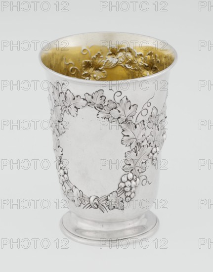 Conical mug, silver on circular foot; belly decorated with relief vine wreaths, one with an English inscription: Carola Kremser / from / SMS/ Nov: 1893. Slightly flared, profiled rim. Gilded interior. Maker: Barnard, Edward & Sons Ltd. Date: 1861–1862. Place: London, England. Vessel. Height 12 cm; diameter 9 cm; weight 175 g., A silver cup with a rounded base and flared rim, the exterior decorated with an embossed grapevine motif including leaves and clusters of grapes, and the interior finished with a gold-toned gilding that shows a raised floral pattern; visible colors include silver, gold, white, and subtle gray shading.