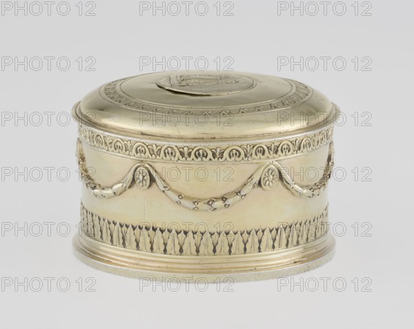 Toilet box, maker: Thomas I Pitts fl. 1755–ca. 1793, goldsmith; style: Classicism/Georgian/George III; date: 1780–1781; place of origin: London, England, Great Britain. Round toilet box with lid, height 5.2 cm, diameter 7.9 cm, weight 206 g. Classicist decoration: laurel festoons suspended from rosette medallions; lower edge with knurled belt of stylized lesbian cymatium; slightly arched cover edged with knurled wavy running dog ornament; central circular medallion with relief of Athena wearing a helmet and holding a spear; right side with a circular reserve and an olive branch. Materials: toilet accessory metalwork., A round decorative box with a domed lid sits against a plain light gray background; the box is a metallic pale gold color with areas of slightly darker golden sheen and subtle tarnish, and it features ornate raised patterns including a band of repeating leaf motifs near the base, a garland-like swag with floral medallions around the body, and an intricately bordered rim b...