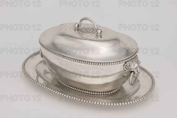 Vase with cover and platter, by Marcin Holke fl. ca. 1765–ca. 1792, goldsmith; tableware elements; vases; 18th century; Poland; Warsaw; vessel; height 20 cm, width 46 cm, depth 31.5 cm, A polished silver covered serving dish with a rounded lid and an arched handle sits on an oval tray; the dish and tray feature a beaded rim detail, the dish has decorative lion head handles with circular rings, and the metal surface shows smooth reflections and subtle scuffs in shades of silver and gray against a pale neutral background.