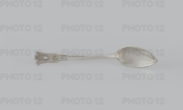 Dessert spoon, Jarra, Marcin 1852–1938 goldsmith, Zakopane style, early 20th century, Kraków, Poland. Dessert spoon with an ovoid, smooth, pointed scoop, a stepped handle ending in a stylized crown and decorated with an engraved geometric ornament stylized to resemble Zakopane style. Cutlery; height 16 cm, width 3 cm, weight 35 g., A single metal spoon lies horizontally on a light gray background, showing a reflective silver color overall with subtle darker gray tarnish spots inside the bowl and along the handle; the bowl is elongated and teardrop-shaped with a smooth interior, while the handle is flat and tapers slightly toward an ornate flared end that features engraved geometric and decorative cutout shapes; the scene contains shades of silver, light gray, and darker gray.
