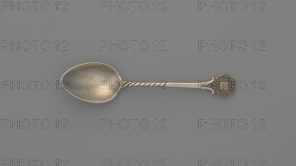 Souvenir spoon, Ford Company fl. 1875–1899 goldsmith's company; Paderewski, Ignacy Jan 1860–1941 - bequest; logos. Souvenir spoon with an ovoid scoop with a pointed tip; half-handle with oblique notches, then flat, splitting at the end with a mounted circular plaque with a struck facsimile of the seal of Yale University in New Haven — in the center an open book with the Hebrew inscription URIM./TUMMIM enclosed in a cartouche around which is the Latin inscription LUX ET VERITAS; inscription around the rim SIGILL: COLL: YALEN: NOV: PORT: NOV: ANGL: Date: 1890s. Place of origin: New Haven, United States of America. Object type: cutlery. Dimensions: height 10.5 cm; width 2.4 cm; weight 15 g., A single metal spoon lies horizontally against a solid medium-gray background, showing a slightly tarnished oval bowl with subtle darker speckles and a warm, muted silver patina; the handle is long and tapers from a twisted midsection into a flattened end that features a round decorative medallion wit...