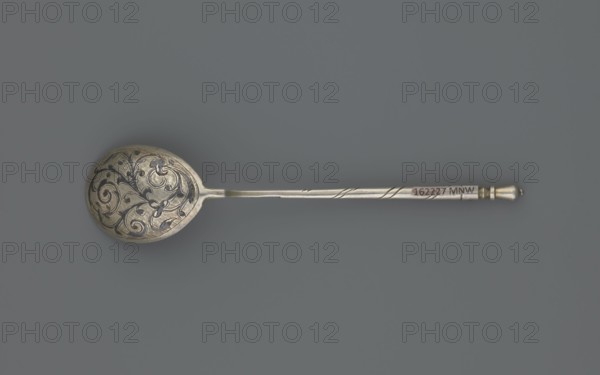 Decorative spoon by Dmitriyev, M fl. 1854–1877, goldsmith. Teardrop-shaped scoop decorated on the reverse with a polished niello acanthus twig; angular handle at the base, becoming conical, ending with a bowl. Dated 1863, Moscow, Russia. Cutlery; height 13 cm, width 2.8 cm, weight 20 g., A single ornate spoon lies horizontally against a solid grey background, showing a rounded bowl with intricate scrolling floral engravings in darker and lighter metallic tones, a long slender handle with subtle twisted grooves and a small bulbous end, the spoon surface reflecting shades of silver, pewter, dark grey, and hints of warm gold.