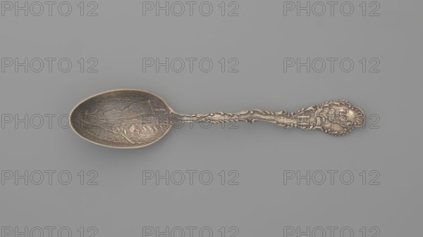 Souvenir spoon, Gorham Mfg. Co. Providence; goldsmith's manufactory; fl. 1865-, Souvenir spoon with an oval scoop with a relief representation of harbor fortifications, bay and ships; at the edge of the scoop the inscription EADS JETTIES. NEW ORLEANS; handle with an irregular edge bordered with acanthus leaves; finial with a portrait of a bearded man and on the sash the signature CAPT. EADS below the breakwater; late 19th century; Providence, United States of America; cutlery; height 14.8 cm, width 3 cm, weight 30 g, A single ornate metal spoon lies horizontally against a plain gray background; the spoon has an oval bowl with an engraved scene and a long decorative handle featuring scrollwork and a raised sculpted figure at the end. The visible colors are metallic tones of brass or bronze with areas of darker patina and the background gray.