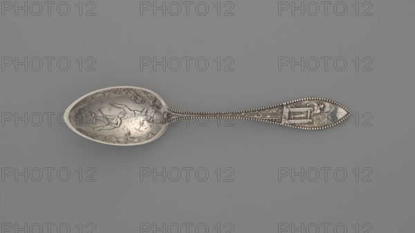 Souvenir spoon, Towle Silversmith fl. 1882-, — souvenir spoon with an ovoid dipper with a pointed tip, showing a scene of the interior of a mine with two men with pickaxes; on the reverse an engraved cursive inscription Batle Mont probably referring to Battle Mount, Nevada. Straight, flaring handle with a lanceolate tip; handle grip depicts a man standing by a well, turning a crank and winding up a chain running along the handle to which a bucket filled with ore is attached, reaching into the mine. On the reverse of the handle a crossed shovel, pickaxe and a rope with an incomprehensible inscription. Late 19th century, Newburyport, United States of America. Materials: cutlery silver. Dimensions: height 14.6 cm, width 2.3 cm, weight 30 g. Made by Towle Silversmith., A metal spoon photographed against a gray background, showing a decorative bowl with an engraved scene and a long ornate handle with bead-like edging; the spoon has overall metallic silver tones with darker engraved areas cr...