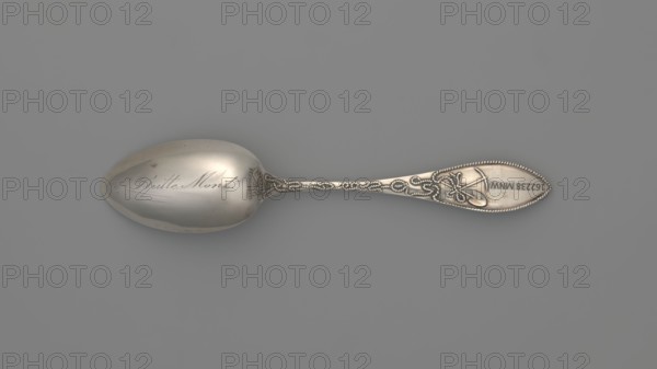 Souvenir spoon by Towle Silversmith fl. 1882–, late 19th century. Ovoid dipper with pointed tip showing a scene of a mine interior with two men with pickaxes; reverse of dipper engraved in cursive Batle Mont probably referring to Battle Mount, Nevada. Straight, flaring handle with lanceolate tip; handle grip depicts a man standing by a well, turning a crank, winding a chain along the handle to which a bucket filled with ore is attached, reaching into the mine. Reverse of handle shows a crossed shovel, pickaxe and a rope with an incomprehensible inscription. Souvenir spoon, cutlery; materials: silver; place of origin: Newburyport, United States of America. Height 14.6 cm, width 2.3 cm, weight 30 g., A single metal spoon lies horizontally on a flat surface, showing a smooth, slightly reflective bowl and an ornate handle with raised decorative patterns; the visible colors are silver tones on the spoon and a muted gray background.