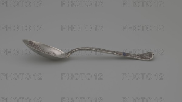 Souvenir spoon, Gorham Mfg. Co. Providence; goldsmith's manufactory; fl. 1865-. Souvenir spoon with an ovoid scoop decorated inside with a relief representation of armament and uniform accessories of the American infantry and cavalry; flat, profiled, widening handle with a heart-shaped tip, edged with twisted wire imitating aglets. Along the handle is the inscription ARMY AND NAVY; above it an enameled United States flag in a cartouche, held in the talons by an eagle with upraised wings, on the wings a sash with the inscription E PLURIBUS UNUM. At the end of the handle, two emblems — the Navy US Navy and the Army US Army of the United States — in circular reserves; on the reverse of the handle, accessories of the United States Navy — an anchor with crossed swords on it, below crossed cannon barrels. Late 19th century. Providence, United States of America. Souvenir, cutlery; height 15 cm, width 3.3 cm, weight 35 g., A single ornate metal spoon lies horizontally on a smooth gray surface,...
