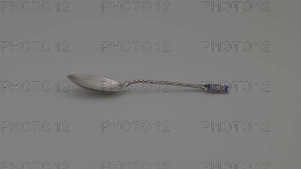 Souvenir spoon, Ford Company fl. 1875–1899. Souvenir spoon with an ovoid scoop with a pointed tip; half-handle with oblique cuts, then flat, splitting at the end, with a plaque attached in the form of a cartouche with an open book bearing the Hebrew inscription URIM/TUMMIM on a background of sapphire enamel. Inscription: Paderewski, Ignacy Jan 1860–1941. Date: 1890s. Place of origin: New Haven, United States of America. Materials/scale: cutlery; length 10.5 cm, width 2.4 cm, weight 15 g., A single metal spoon lies on a smooth surface, showing a reflective bowl with a slightly worn texture and a twisted section along the handle; the handle ends with a small rectangular decorative panel that includes a darker colored inset. The visible colors are silver, gray, and a small area of blue on the handle.