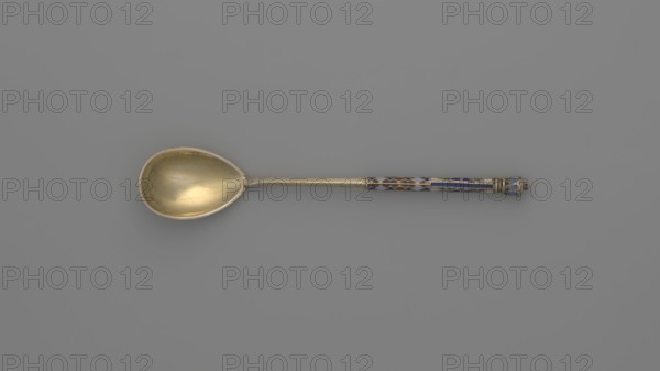 Souvenir spoon by Nikolai Struliev fl. 1886–ca. 1910, goldsmith. Decorative spoon with teardrop-shaped scoop and angular handle, half decorated with a geometric ornament in colored cellular enamel, topped with a bowl. Dated 1886–1894, Moscow, Russia. Cutlery; height 12.5 cm, weight 20 g., A single spoon lies horizontally against a plain gray background; the bowl of the spoon is metallic with a warm golden tone and shows a smooth, slightly reflective surface with subtle scratches, while the long handle transitions to a decorative section near the end featuring enamel inlays in blue and red set within metallic borders, and the very end has a small turned finial with blue enamel accents.