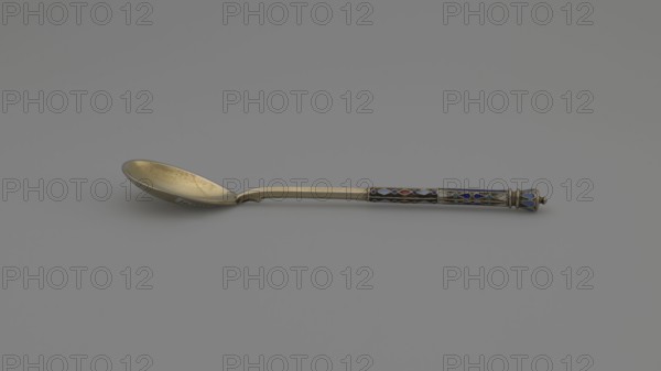 Souvenir spoon by Nikolai Struliev fl. 1886–ca. 1910, goldsmith. Decorative spoon with teardrop-shaped scoop and angular handle, half decorated with a geometric ornament in colored cellular enamel, topped with a bowl. Dated 1886–1894, Moscow, Russia. Cutlery; height 12.5 cm, weight 20 g., A metal spoon rests on a gray surface and background; the bowl of the spoon is gold-toned with a slightly worn, speckled interior and a smooth rounded shape, leading to a narrow gold-toned stem that transitions to a decorated handle. The handle features a patterned section with enamel-like inlays in blue, dark blue, red, and turquoise set against metallic outlines, and it ends in a slightly bulbous, ornamental finial with blue and metallic tones. Overall visible colors include gray, gold, blue, dark blue, red, turquoise, and metallic silver.