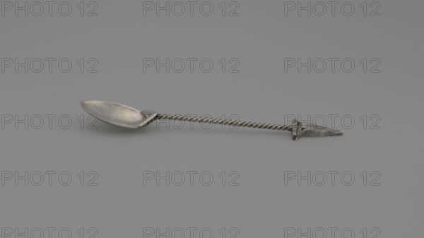 Souvenir spoon, subject: Ignacy Jan Paderewski 1860–1941 — souvenir from Paderewski's tour of Australia and New Zealand in 1904. Early 20th century before 1904. Materials and form: egg-shaped scoop with a pointed tip; twisted wire handle topped with a semi-plastic kangaroo. Motif: Australian fauna kangaroos. Type: cutlery, varia. Dimensions: length 12.5 cm, width 2.2 cm, weight 15 g., A single metal spoon lies horizontally on a smooth background, showing a shallow oval bowl with subtle surface marks and a twisted handle extending to a decorative terminal; the visible colors are shades of silver and gray with faint slightly warmer reflections on the bowl and a uniformly gray backdrop.