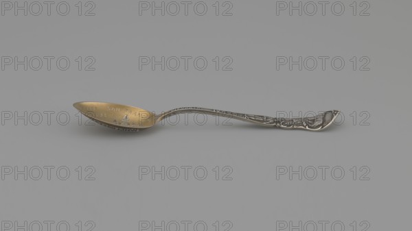 Souvenir spoon, Mechanics Sterling Co. Attleboro; goldsmith's firm; fl. 1896–1955. Souvenir spoon with ovoid scoop, gilded, decorated with an engraved representation of a Victorian-style building resembling a French chateau built on a rock in 1896 burned down in 1907 with the inscription in italics SAN FRANCISCO CLIFF/HOUSE; a widening handle with a profiled edge decorated with a relief ornament on both sides, on one side an inscription along the handle CALIFORNIA 1849 adoption of the California Constitution and the beginning of the gold rush, above it a gold prospector; in the finial a bear symbolizing the state of California; on the reverse fruit characteristic of California; in the finial the state emblem — a seated Minerva, next to her a lying bear, with a background landscape. Date: 1896–1907. Place of origin: United States Attleboro. Classification: cutlery. Dimensions: length 10 cm, width 2 cm, weight 5 g. Maker: Mechanics Sterling Co., A single ornate spoon lies horizontally ag...