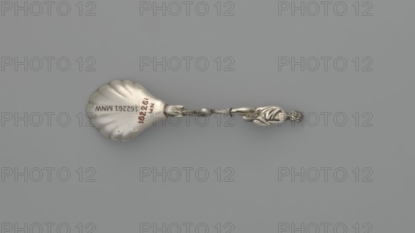 Decorative silver spoon, shell-shaped scoop, handle formed by a solid dolphin supporting a naked woman who covers her breasts with her left hand and holds a shawl to cover her womb with her right; embellished with Venus and dolphin symbolism. Maker: François-Auguste Boyer-Callot fl. 1865– . 4th quarter of the 19th century, Paris, France. Cutlery; length 8.5 cm, width 2.4 cm, weight 10 g., A metal spoon with a scallop-shaped bowl and a decorative twisted handle ending in a small sculpted figure is shown on a plain background; the spoon appears silver in color with some darker tarnished areas, and the background is gray.