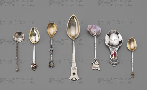 Souvenir spoon, Paderewski, Ignacy Jan 1860–1941. Souvenir spoon with a scoop from the papal medal of Pius VI minted on the occasion of the anniversary of the pontificate, depicting on the obverse the head of the pope with the inscription on the rim PIVS SEXTVS PONT MVI and on the reverse a representation of the personification of abundance Abundantia? and the partially preserved rim inscription DE SANCTO 1780.... 19th century, Italy. Cutlery, varia. Length 9.5 cm; width 2.3 cm; weight 10 g., A row of several decorative spoons is arranged horizontally on a flat gray background, showing a variety of bowl shapes and handle designs; colors visible include silver, gold, purple, red, blue, green, and hints of brown and black. The spoons feature a mix of polished metallic surfaces and ornate handles, with a few twisted metal stems, a group of enameled and bejeweled embellishments, a scallop-shaped bowl with purple tones, a large elongated bowl with a gold-toned interior, and a round bowl wit...