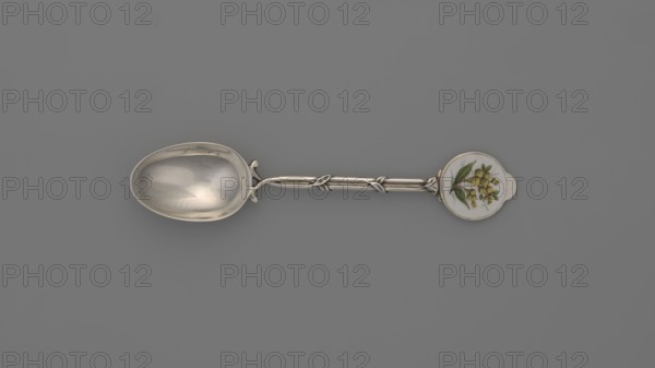 Decorative spoon by Deakin & Francis Ltd Birmingham; goldsmiths; fl. from 1786. Spoon with an ovoid smooth scoop; handle formed of two intertwined stylized branches with leaves, ending in a round flat terminal with enameled decoration depicting on a white background a branch with yellow spherical fruits and lanceolate green leaves. Inscribed/linked to Paderewski, Ignacy Jan 1860–1941. England, Birmingham, Great Britain, 1912/1913. Cutlery; height 11.5 cm, width 2.4 cm, weight 15 g., A silver spoon laid horizontally on a gray background with an oval bowl on the left showing reflective silver surfaces and subtle scratches, a decorative silver handle with twisted and knotted elements in the middle, and a round decorative end on the right featuring a white circular inset painted with a botanical motif of green leaves and small yellow berries; visible colors include gray, silver, white, green, and yellow.