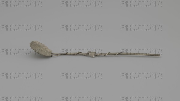 Decorative spoon, decorative spoon with a flat round scoop with irregular edges decorated on both sides with engraved leaves and clusters; flat handle simulating a branch around which a vine is entwined; late 19th century; vines; cutlery; varia; height 14 cm; width 2.5 cm; weight 5 g., A long slender metal spoon with a decorative scalloped bowl at one end and a twisted handle running its length, the handle featuring a small leaf-shaped ornament; the spoon and background show shades of gray and muted silver.