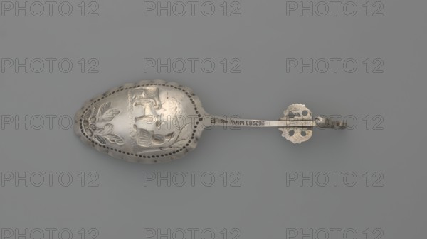 Decorative spoon, decorative spoon with an oval scoop featuring a relief pastoral scene framed by a pearled border — a woman sits under a tree with two sheep beside her; floral decoration at the bottom; irregular, wavy scoop edge. Flat handle with a volute ending, decorated with an openwork section depicting a winged putto head and a sculpted lion standing on its hind legs. Late 19th century, Netherlands. Cutlery; height 14 cm, width 4.3 cm, weight 20 g., A metal spoon lying flat on a neutral gray background, showing a decorative bowl with embossed designs including floral motifs and a scene with an animal and a small human-like figure, surrounded by a perforated border; the handle is slender and leads to an ornate looped end with cutout shapes and a small attached ring. The visible colors are silver tones of the metal and various shades of gray in the background and on the spoon's surface.