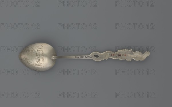Souvenir spoon, Paderewski, Ignacy Jan 1860-1941 - testament provenance, Japanese dragon motif, Silver souvenir spoon with a teardrop-shaped scoop decorated with an engraved stylized peony flower, Japanese inscription on the reverse, below it the Latin alphabet NAGASAKI; narrow half-cylinder handle topped with a half-plastic Japanese dragon with three claws, late 19th century, Asia, Far East, cutlery, varia, length 15 cm, width 3 cm, weight 15 g, A metal spoon lies flat against a smooth gray background, showing a slightly tarnished silvery surface with worn areas and scratches. The bowl of the spoon is rounded and has engraved decorative marks and shallow incised lines, while the handle is long and narrow with a flattened central section that transitions into a more ornate, irregularly shaped end with scalloped and jagged edges. The overall colors visible are silvery metal tones with darker gray tarnish, and the background is a uniform medium gray.