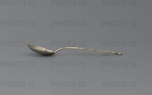 Souvenir spoon, Paderewski, Ignacy Jan 1860-1941 creator unknown, Silver souvenir spoon with a teardrop-shaped scoop decorated with an engraved stylized peony flower; Japanese inscription on the reverse, below it the Latin alphabet NAGASAKI; narrow half-cylinder handle topped with a half-plastic Japanese dragon with three claws. Late 19th century. Asia, Far East. Cutlery, varia. Length 15 cm, width 3 cm, weight 15 g., A single metal spoon rests on a smooth flat surface, showing a shallow, rounded bowl with decorative scalloped patterns along its rim and a curved handle that tapers and appears textured and slightly irregular; the spoon and the scene are in shades of metallic silver and gray against a mid-gray background.