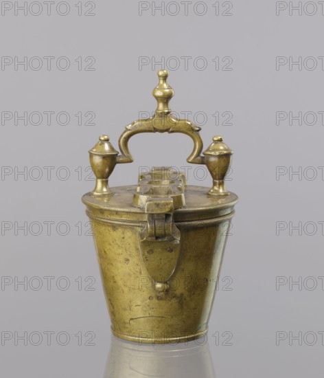 Seven weights in the form of bowls—truncated cones; the eighth, largest, serves as a container for the others and has a hinged lid with a movable handle mounted in pinnacles shaped like simplified vases. On the lid: stamped 16 MARK, Prussian eagle, BERLIN stamp; another mark engraved 160; on the side engraved 152. Late 18th century, Germany. Maker: Gwicht unknown role of the creator. Materials: measures and weights., A small metallic container with a hinged lid and ornate handle sits centered against a pale gray background; the object is brass-colored with a slightly aged patina and shows areas of darker tarnish and subtle scratches, the lid topped by a decorative finial and two small urn-shaped knobs, a curved handle with sculpted details arches between them, and the tapered body has a smooth surface with a few small dents and a rounded base that reflects faintly onto the surface beneath.