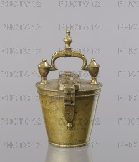 Seven weights in the form of bowls—truncated cones; the eighth largest serves as a container for the others, with a hinged lid; closed with a lid; with a movable handle mounted in pinnacles shaped as simplified vases. On the lid stamped 16 MARK, Prussian eagle, BERLIN stamp; 160 engraved on another mark; on the side engraved 152. Late 18th century, Europe, Germany. Weight. Maker: Gwicht, Szewczykowski, Roman 1849–1901., A small metallic container with a hinged lid and a decorative handle sits against a plain gray background. The object is brass-colored with a slightly worn, patinated surface showing darker and lighter areas. The lid features a central ornate arching handle with a rounded finial and two smaller urn-shaped finials on either side. The top also has a raised, stepped section with circular openings. A latch extends down the front of the container from the lid to the body. The body tapers inward toward the base and shows subtle surface marks and scratches. The reflection of t...