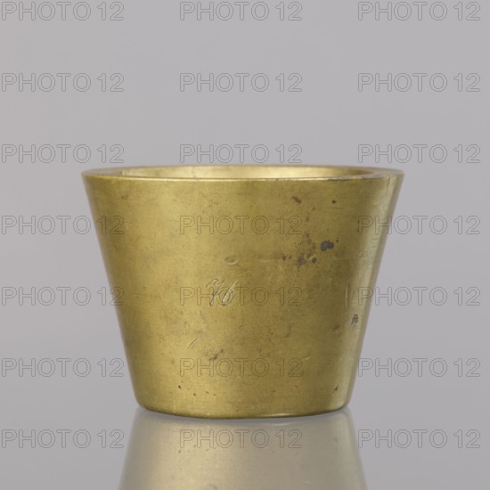 Gwicht, unknown creator; Szewczykowski, Roman 1849–1901 author; measures and weights; object in the shape of a truncated cone with markings: 4 M engraved inside and on the side 76; weight 935.18 g; end of 18th century; Germany; height 6.2 cm; width 8.6 cm, A small metallic cup with a tapered shape sits centered against a smooth light gray background, displaying a warm brass color with areas of darker tarnish and small blemishes; the rim shows slight wear and the interior reflects a similar golden hue, while the base rests on a reflective surface that mirrors a muted version of the brass and surrounding gray.