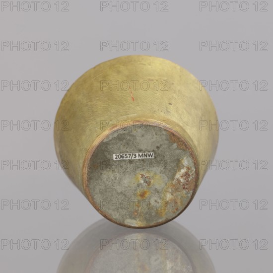 Gwicht; creator, Szewczykowski, Roman 1849–1901 noted in provenance; ; measures and weights; object in the shape of a truncated cone; no markings; bottom surface covered with a layer of tin; weight 410.2 g; late 18th century; dimensions: height 4.9 cm, width 6.9 cm., A rounded object resting on a reflective surface, showing the underside with a circular base; the exterior surface is a muted yellow-gold with subtle variations and small spots of reddish discoloration, while the base shows a weathered gray area with mottled patches of rusty orange and pale yellow; the background is a uniform light gray.