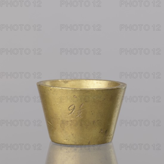 Gwicht; creator, Szewczykowski, Roman 1849–1901 provenance/gift; measures and weights; in the shape of a truncated cone; engraved marking on the side 91/2, inside 8, eagle; 116.45 g; end of 18th century; Europe; Germany; weight; height 2.9 cm; width 4.5 cm, A small metallic cup with a tapered cylindrical shape sits centered on a reflective surface; the cup has a worn golden color with areas of darker patina and a few small spots of discoloration, and the interior shares the same golden hue; the background is a uniform light gray.