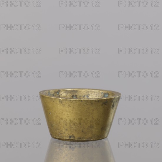 Gwicht, unknown creator; Szewczykowski, Roman 1849–1901 — ; measures and weights; in the shape of a truncated cone; markings on the side engraved 43/4, inside 4, eagle; 57.84 g; 18th century; Europe; Germany; weight; height 2 cm; width 3.8 cm, A small metal cup with a wide top tapering to a narrower base sits on a reflective surface, showing a worn, uneven texture with small spots of discoloration; the cup appears in shades of gold and brass with hints of darker greenish-blue patina, and the background is a smooth light gray.