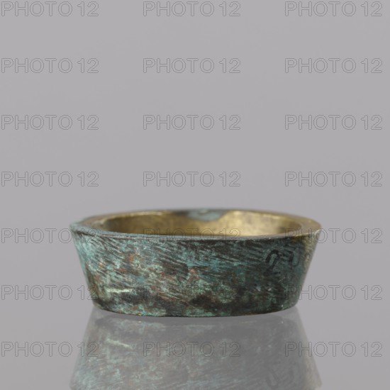 Gwicht, unknown creator; Szewczykowski, Roman 1849–1901 - ; In the shape of a truncated cone; internal marking 2; weight 24.75 g; 18th century; Europe; Germany; height 1 cm; width 3.1 cm., A shallow, round metal bowl with a weathered greenish-blue patina on its exterior and a warm golden interior sits on a reflective surface, showing a muted reflection; the bowl displays textured, irregular surface marks and variations in green, blue, brown, and gold tones against a plain light gray background.