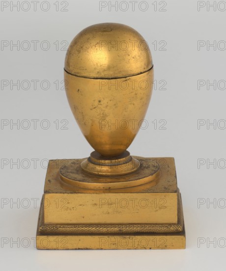 Inkwell, creator Tadeusz Bylewski 1866–1939, early 19th century, France, inkwell; height 13.5 cm, width 9.4 cm, depth 8.4 cm, A gilded object with a rounded, egg-shaped top sitting on a pedestal base, showing worn and mottled gold surfaces with darker scuffs and spots; the egg-shaped portion has a visible seam near its upper third and a smooth curved profile that narrows toward a circular plinth, which rests on layered, stepped platforms; the square base features a textured band along its upper edge and flat faces that exhibit similar wear and muted gold tones; the background is a neutral pale gray.
